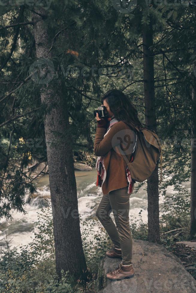 Capturing the view. Full Length of young modern woman with backpack photographing nature while hiking in the woods photo