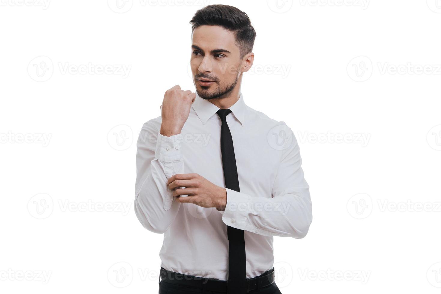 Getting dressed. Good looking young man in white shirt and tie adjusting his sleeve while standing against grey background photo