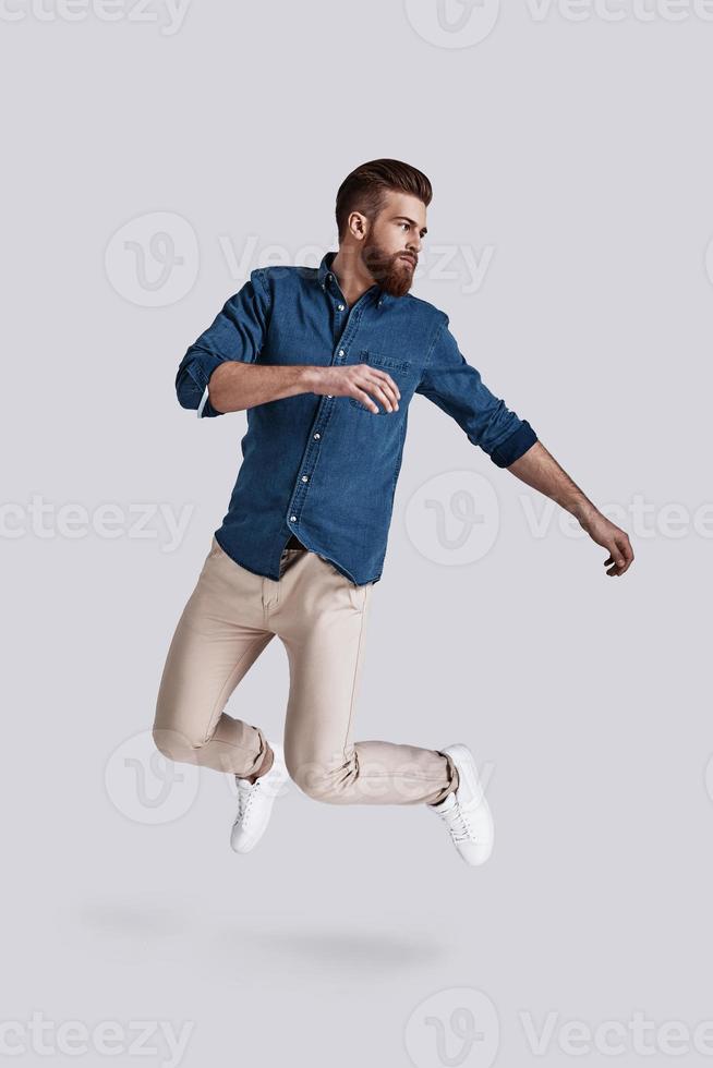 Feeling comfortable in his style.  Full length of handsome young man looking away while jumping against grey background photo