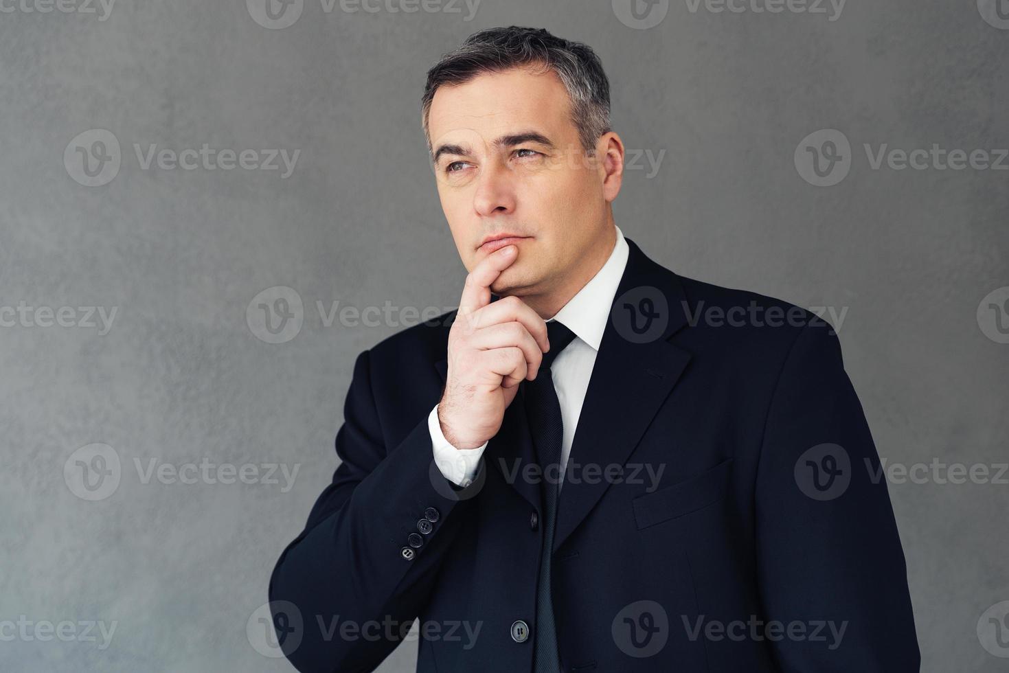 Finding perfect solution. Mature businessman holding hand on chin and looking thoughtful while standing against grey background photo