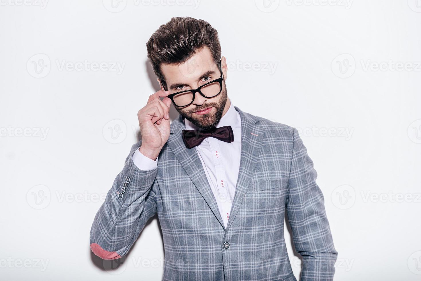 Well hello Close-up of handsome young confident man wearing suit looking over his glasses while standing against white background photo