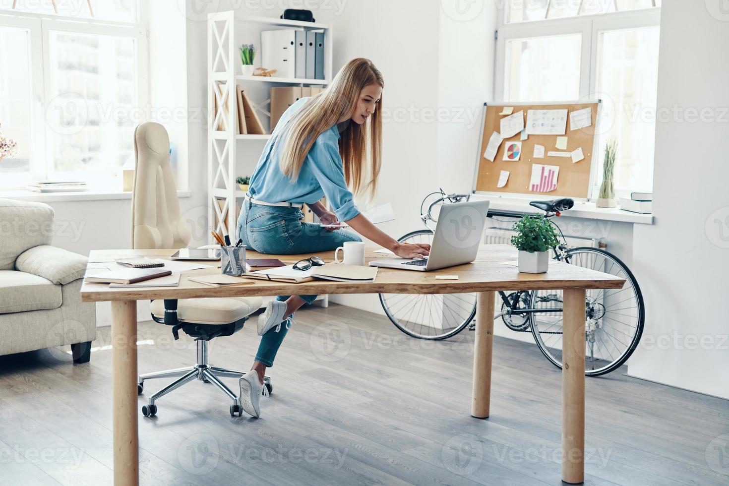 Beautiful young woman in smart casual wear using laptop while working in the office photo