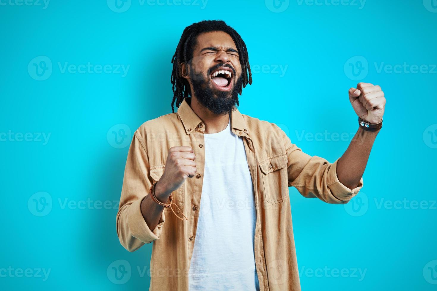 Handsome young African man in casual clothing cheering and shouting while standing against blue background photo