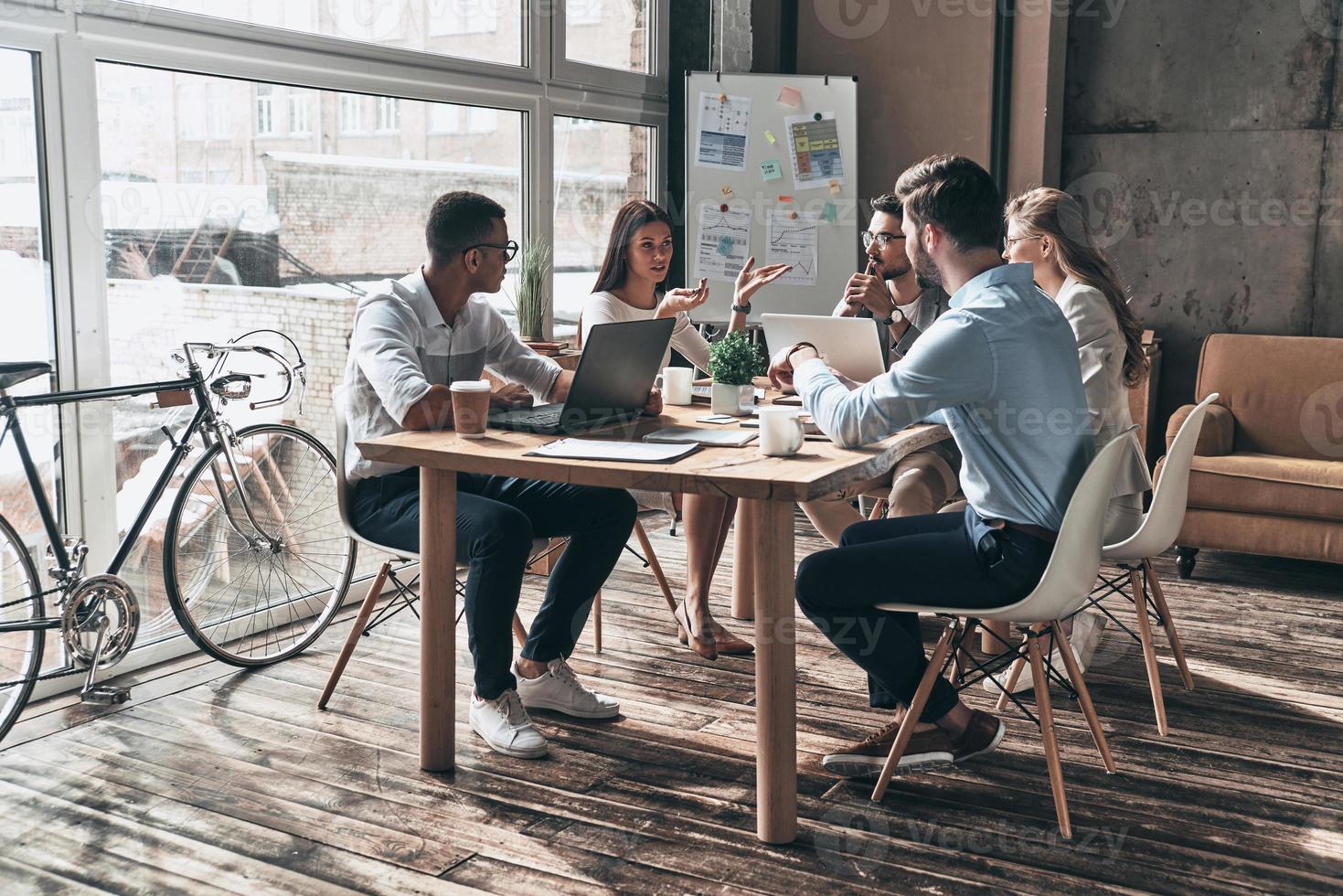 Working day. Group of young modern people in smart casual wear discussing business while working in the creative office photo