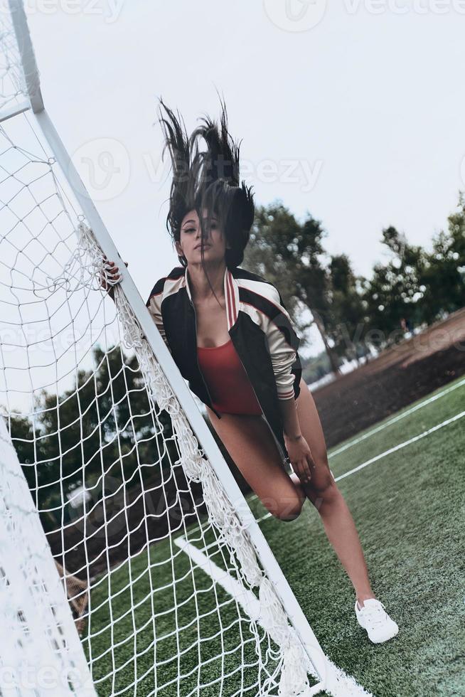 belleza deportiva. toda la longitud de una joven atractiva en bikini rojo posando cerca del poste de gol en el campo de fútbol foto