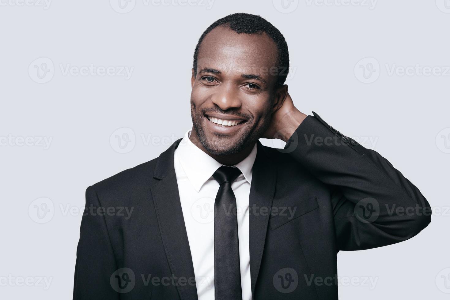 Handsome businessman. Portrait of confident young African man holding hand behind head and smiling while standing against grey background photo