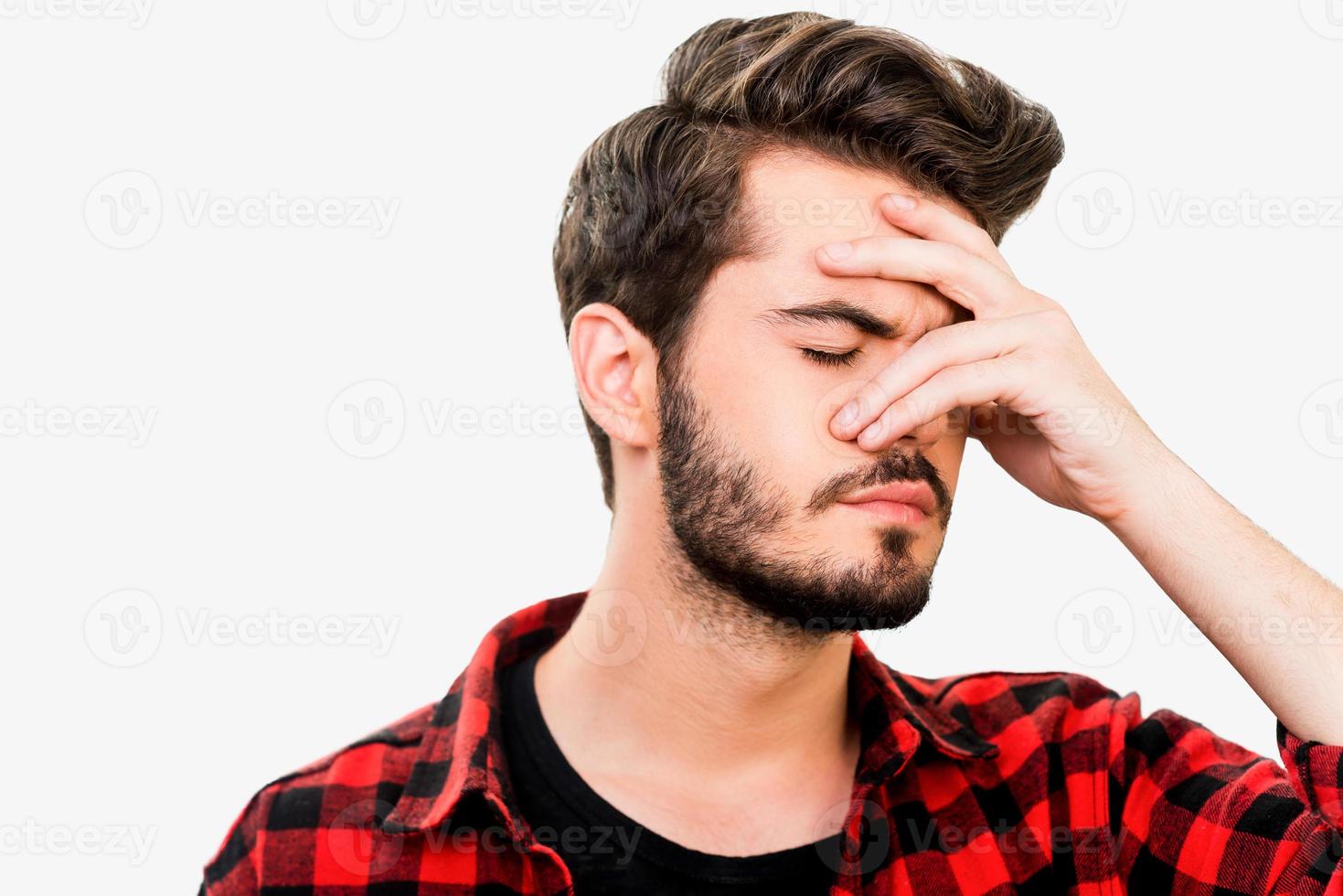 Too stressful day. Frustrated young man keeping eyes closed and covering his face by hand while standing against white background photo