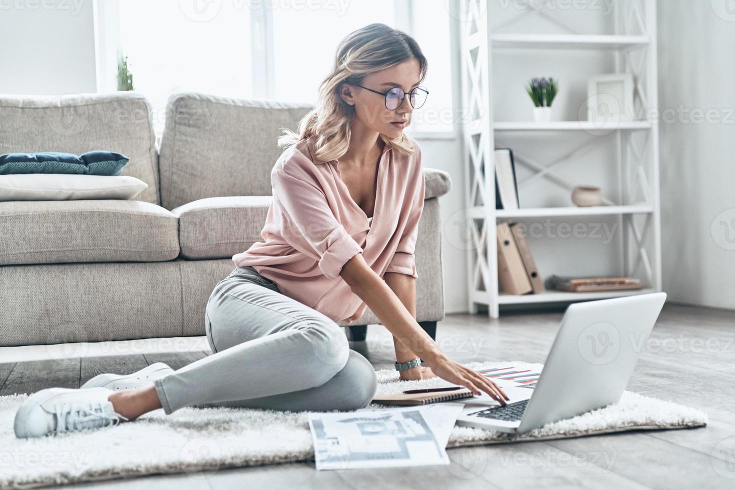 Young and full of ideas. Thoughtful young woman in eyewear working using computer while flooring at home photo