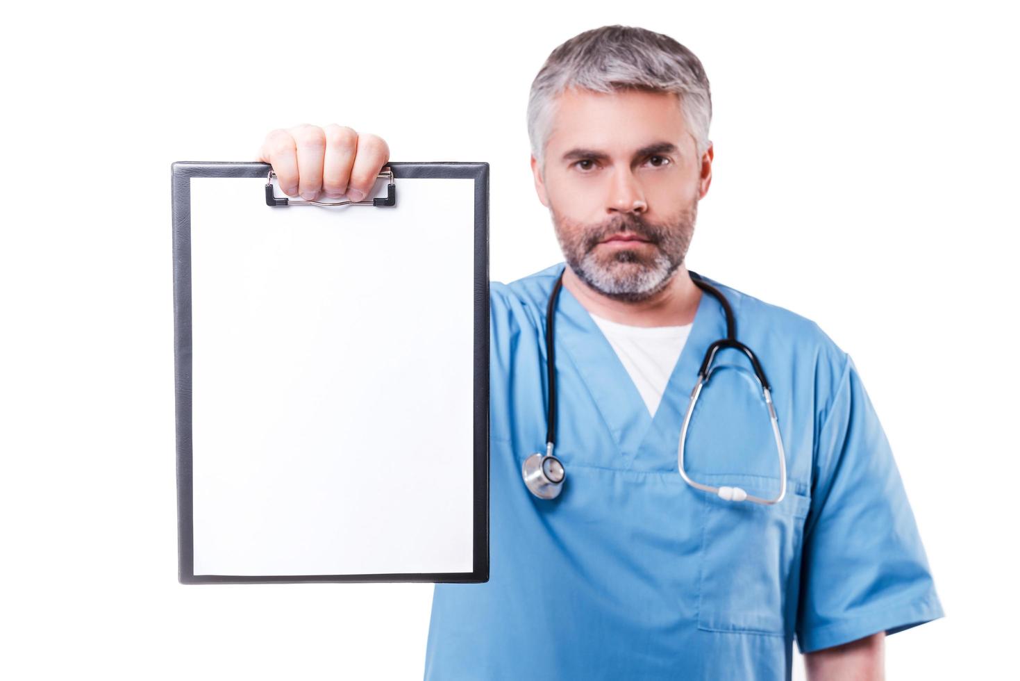 Copy space on his clipboard. Confident mature doctor looking at camera and showing clipboard with copy space on it while standing isolated on white photo