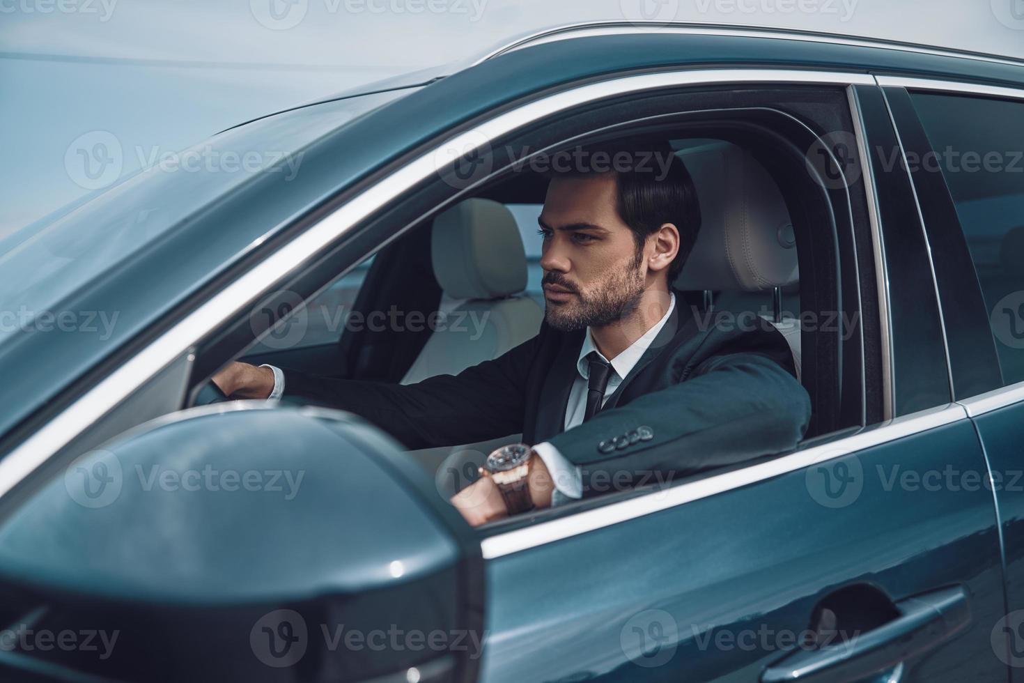 solo sigue moviéndote, un joven apuesto con traje completo mirando directamente mientras conduces un auto foto