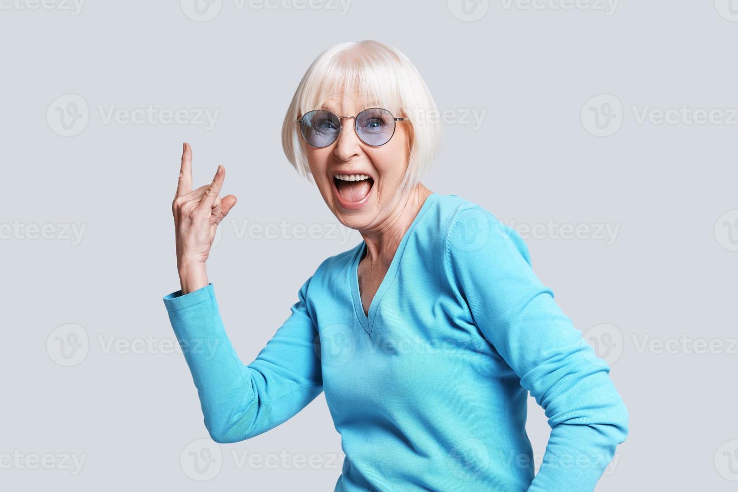 Rock it Playful senior woman making rock on sign and smiling while standing against grey background photo