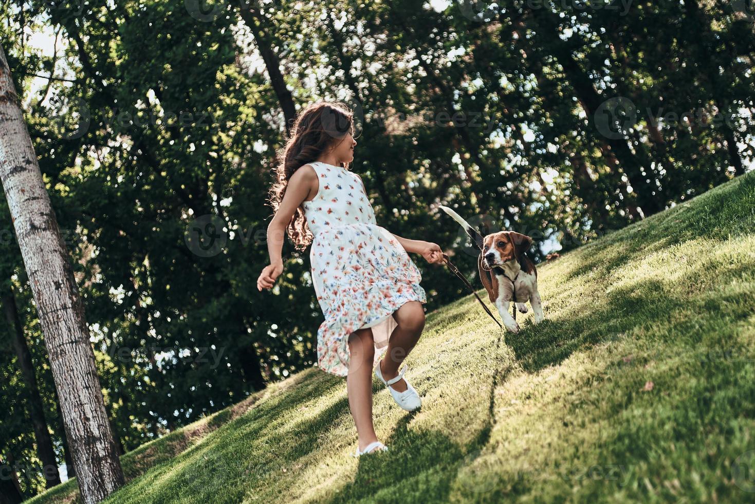 toda la longitud de una linda niña jugando con su perro mientras corre al aire libre foto