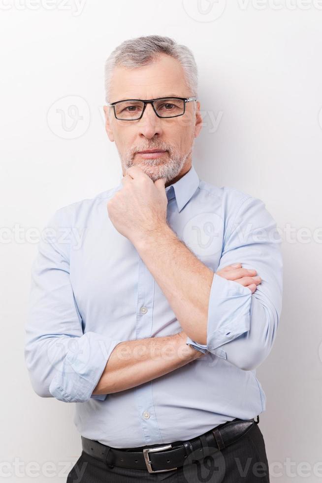 Thinking about your problem. Thoughtful senior man in formalwear holding hand on chin and looking at camera while standing against white background photo