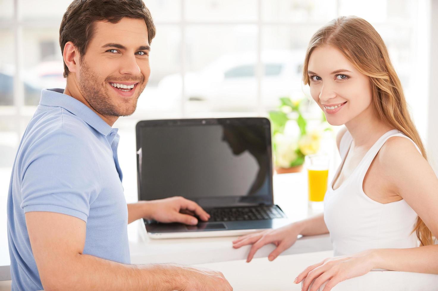 Surfing the net together. Handsome young man sitting at the table and using laptop while his girlfriend standing behind him photo