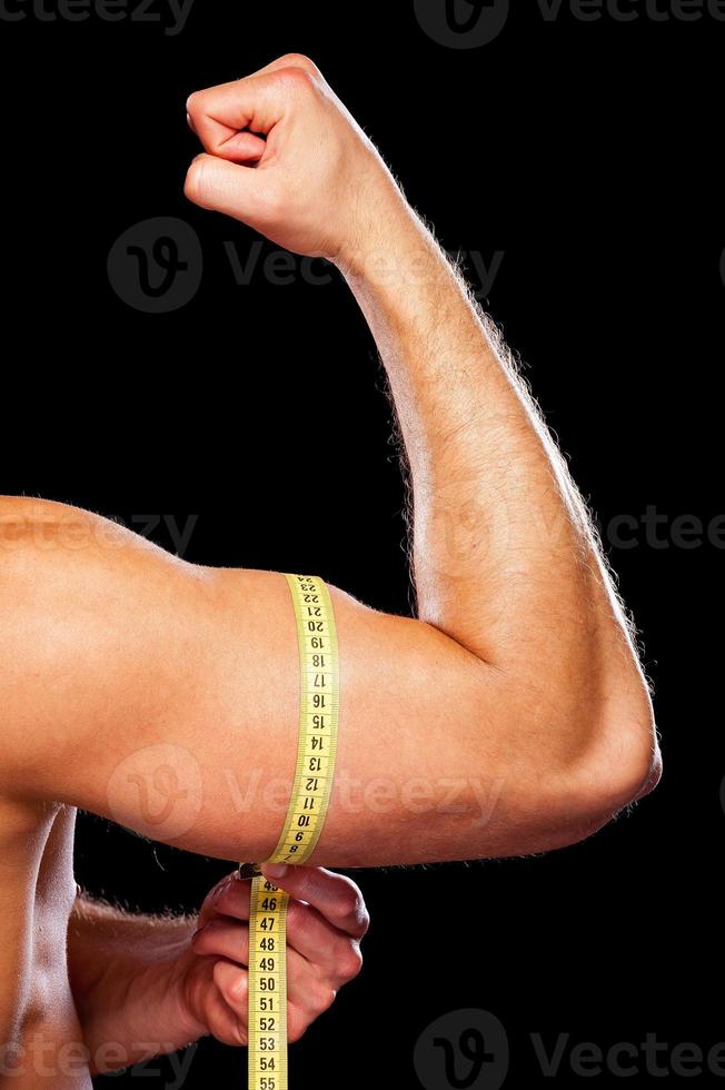 Measuring his perfect bicep. Closeup of muscular man measuring his bicep with measuring tape