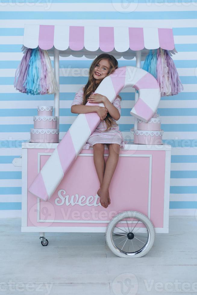 Cute little girl looking at camera and smiling while sitting on the candy cart decoration photo