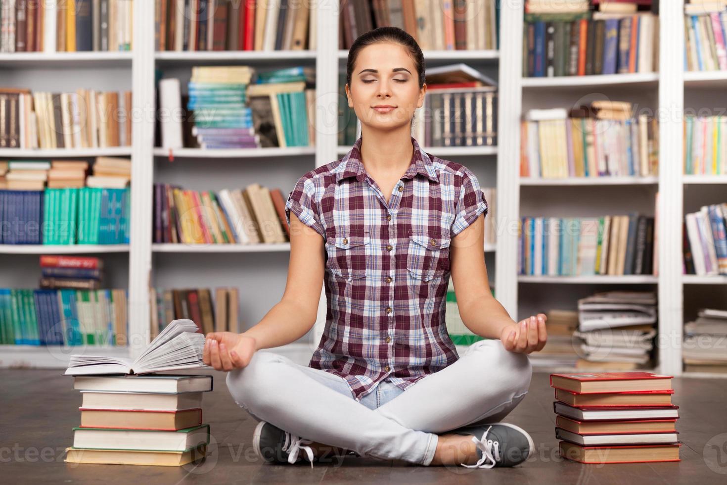 Time to chill. Beautiful young woman keeping her eyes closed and meditating while sitting at the library photo