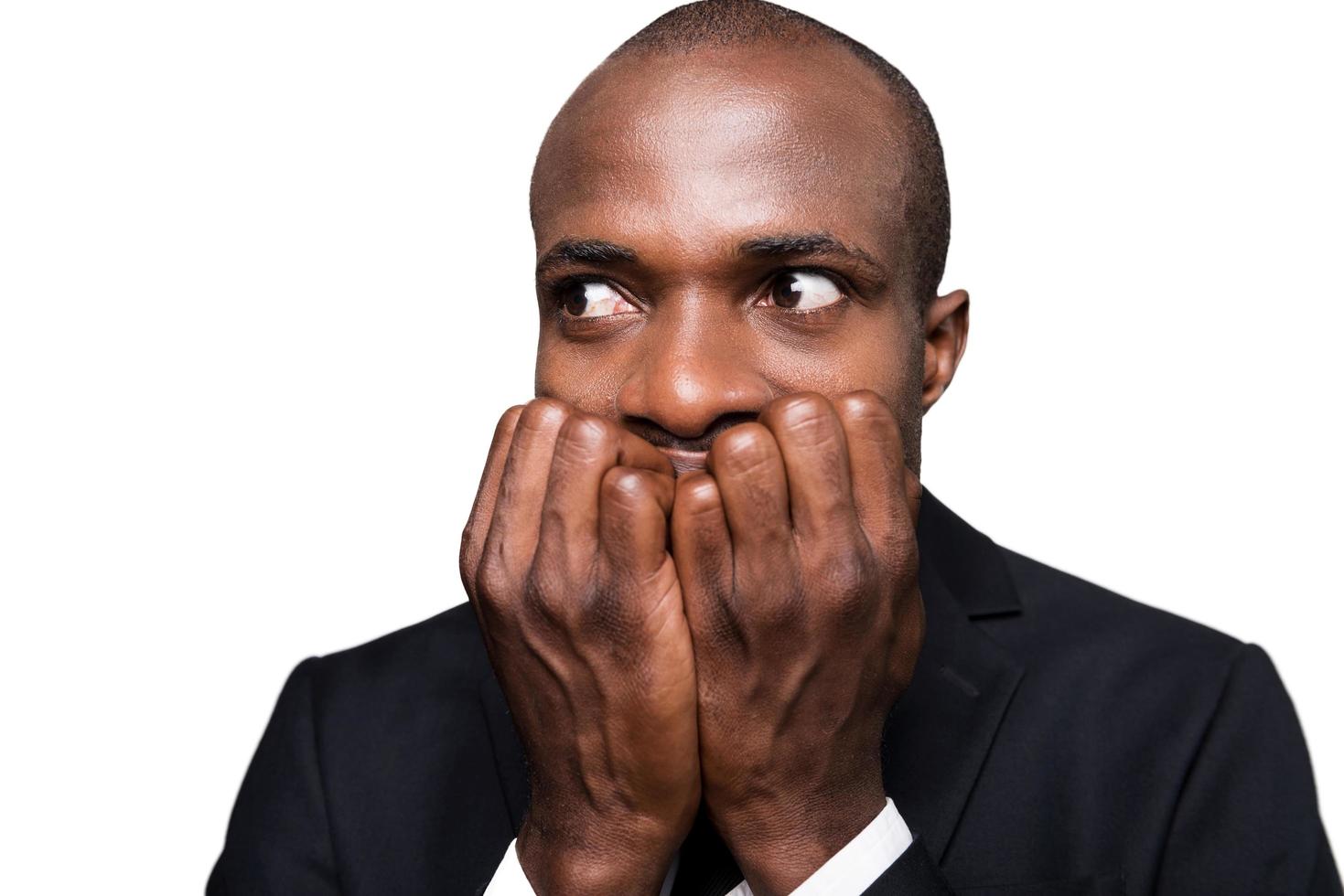 Terrified businessman. Terrified young African man in formalwear holding fingers in mouth and looking away while standing isolated on white background photo