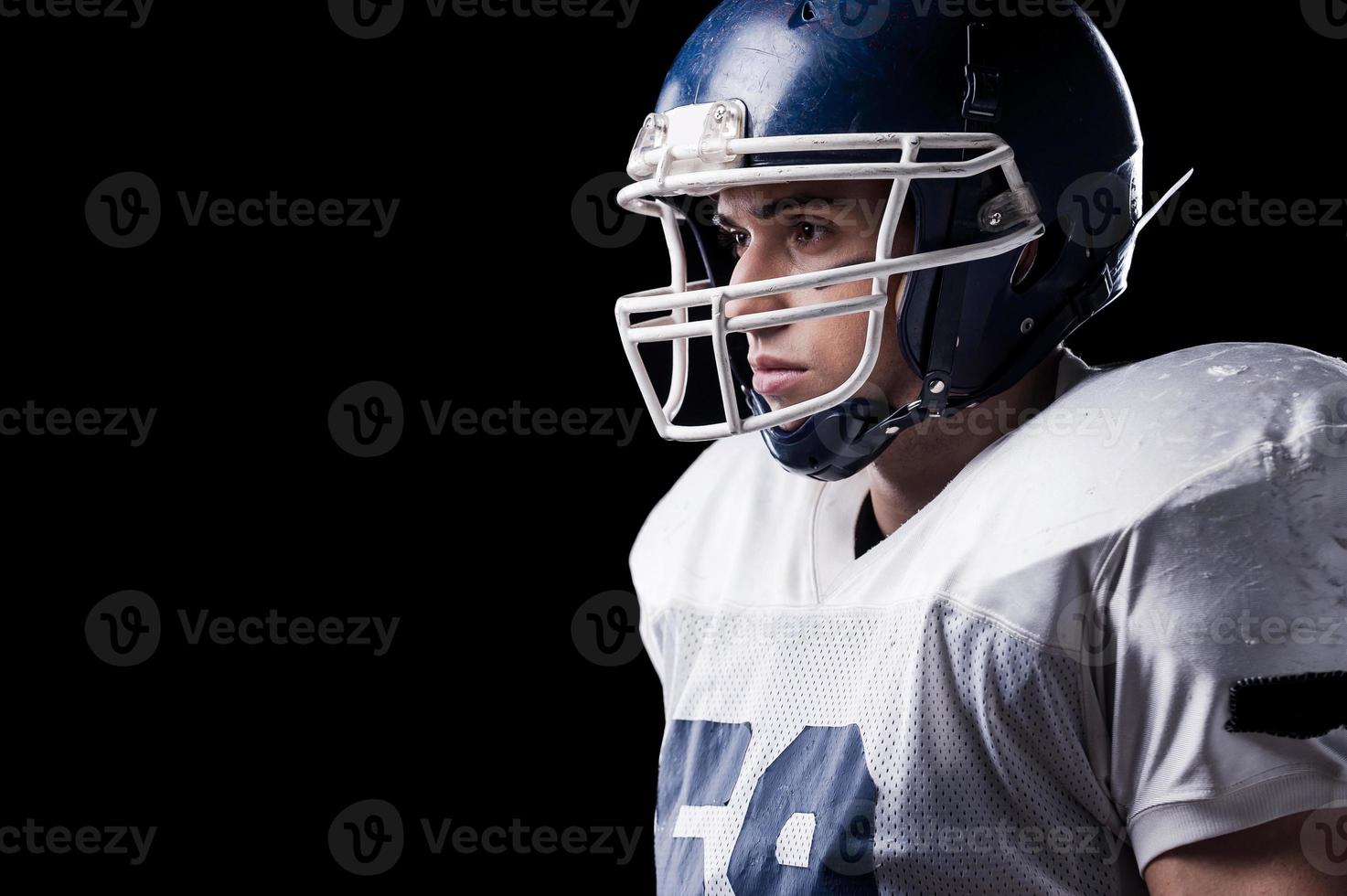 Concentrated on game.  Side view of American football player looking away while standing against black background photo