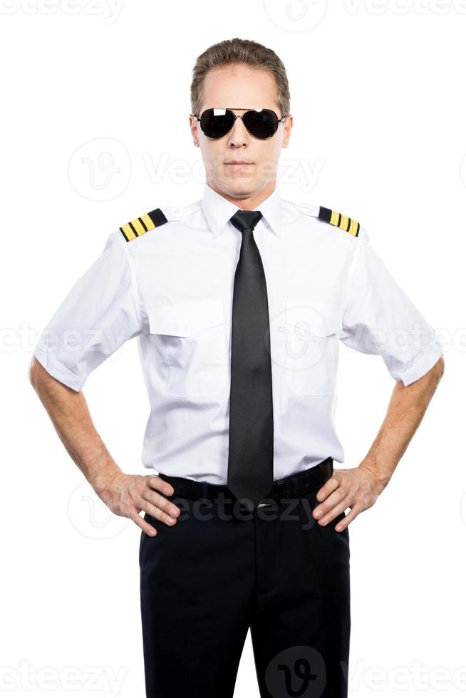 Confident and experienced pilot. Confident male pilot in uniform holding hands on hip while standing against white background photo