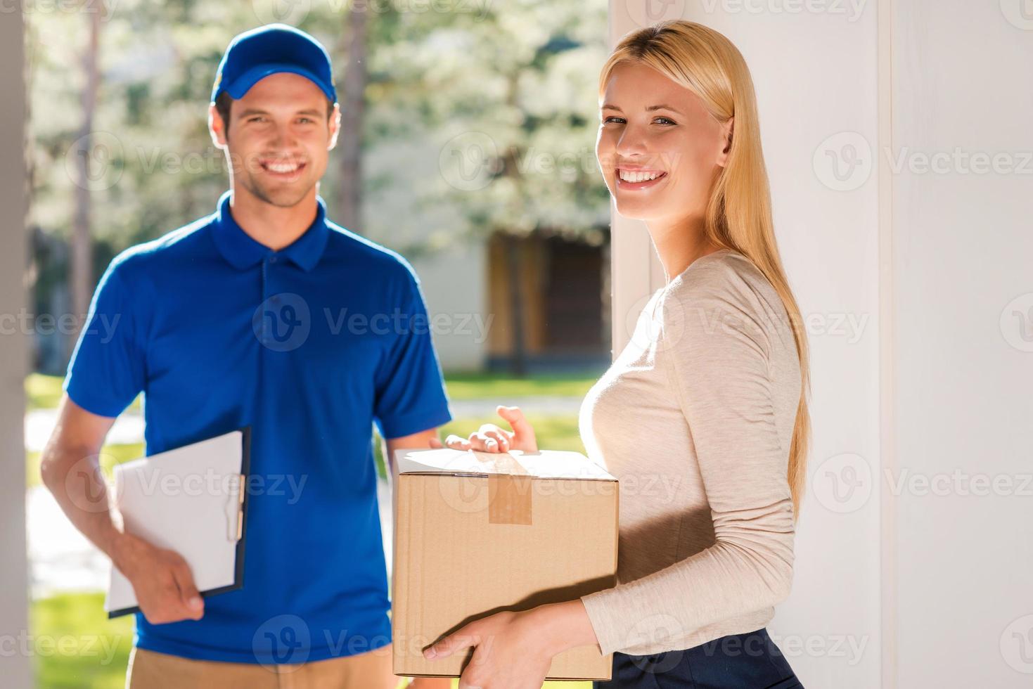 First class delivery service. Beautiful young woman holding a cardboard box while young delivery manholding clipboard and smiling photo