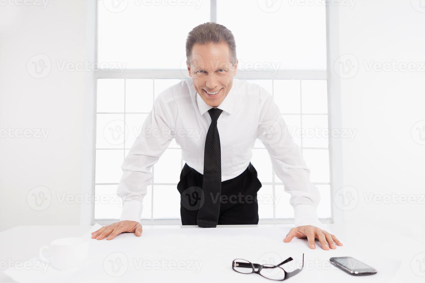 arquitecto en el trabajo. un anciano alegre con camisa y corbata apoyado en la mesa con un plano encima foto