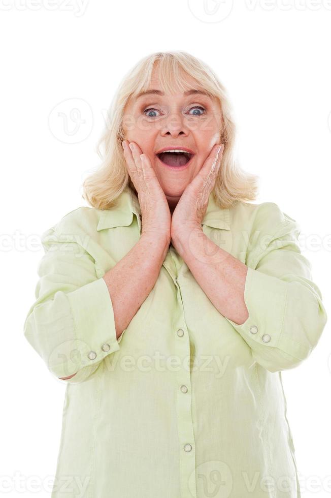 Qué sorpresa, una anciana feliz sosteniendo la cabeza entre las manos y expresando positividad mientras estaba aislada en el fondo blanco foto