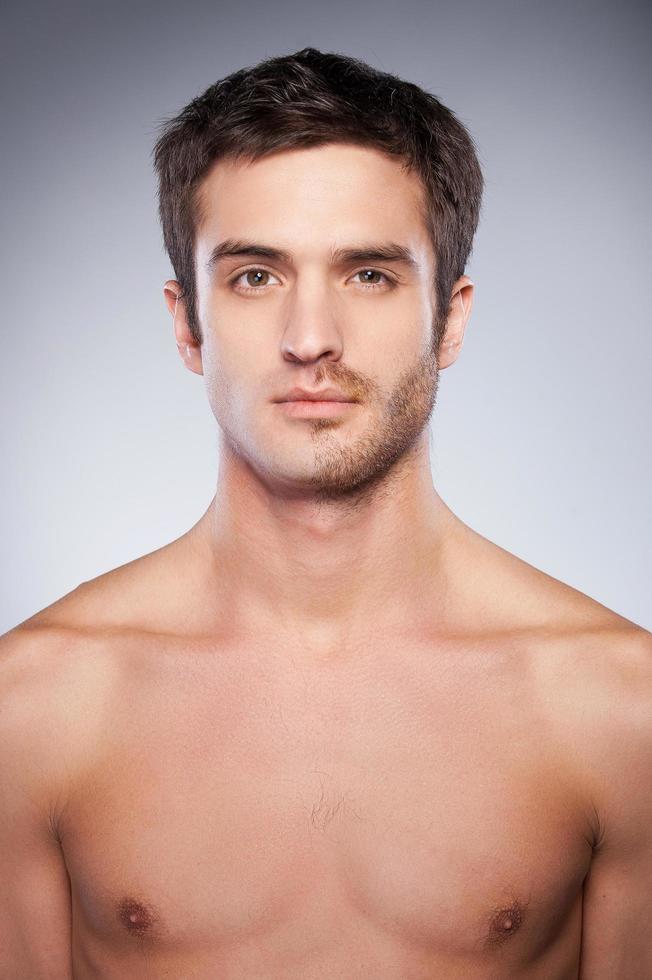 medio afeitado. hombre joven guapo con la cara medio afeitada mirando a la cámara mientras está de pie contra el fondo gris foto