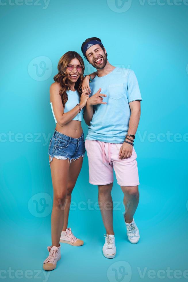 Full length of beautiful young couple embracing and smiling while standing against blue background photo