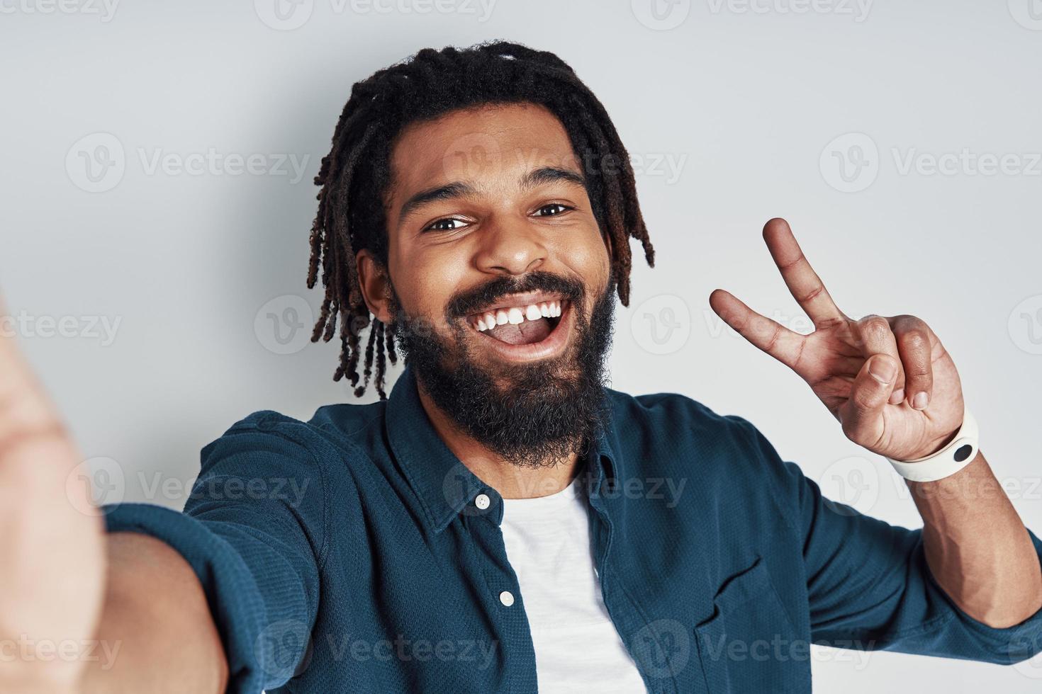 Self portrait of handsome young African man looking at camera and smiling while standing against grey background photo