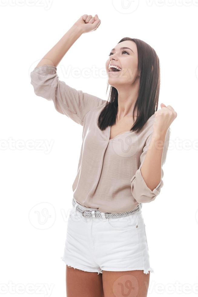 ganador de todos los días. hermosa mujer joven en ropa casual elegante gesticulando y luciendo feliz mientras está de pie contra el fondo blanco foto