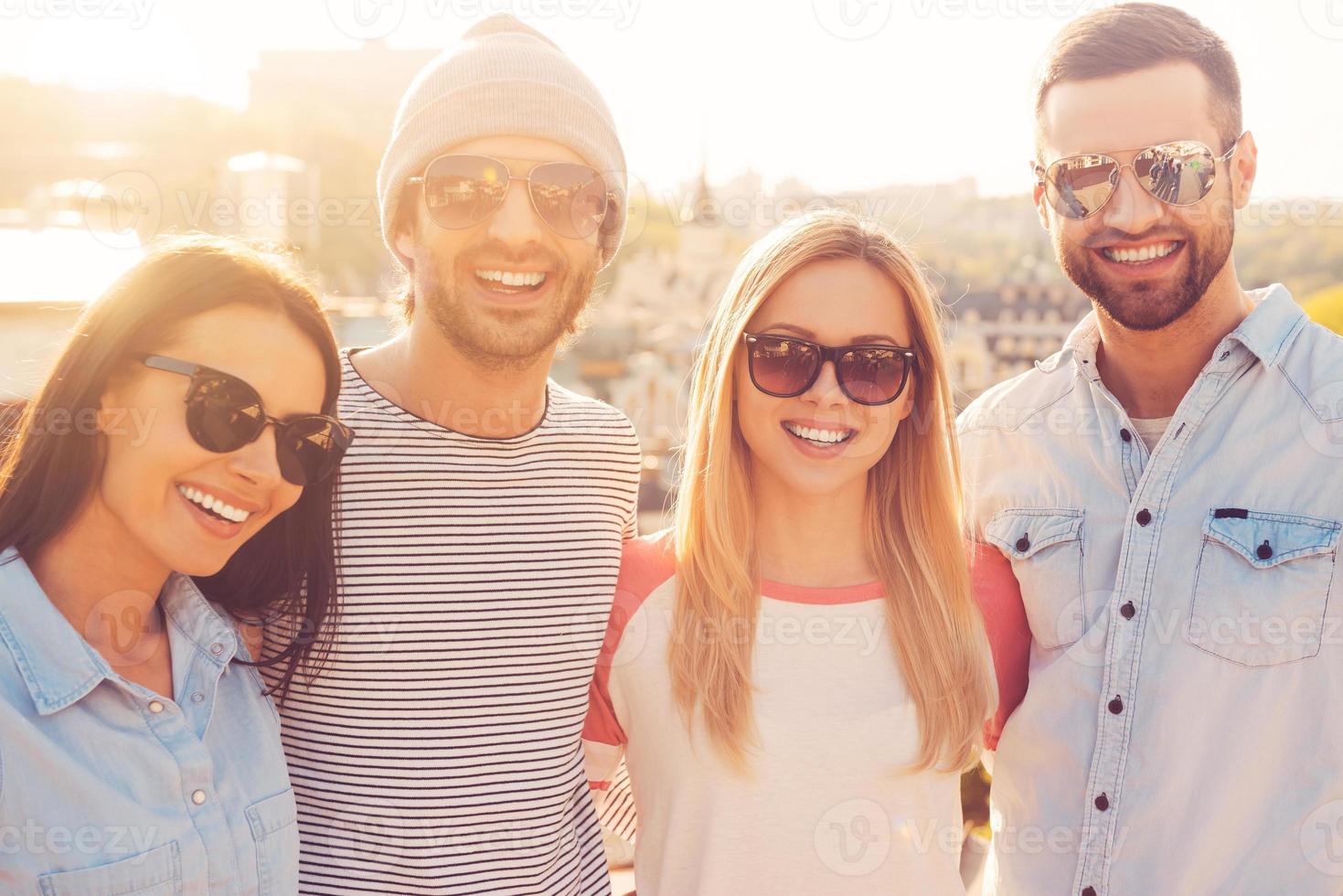The best friends ever. Four young cheerful people bonding to each other and smiling while standing close to each other with great cityscape in the background photo