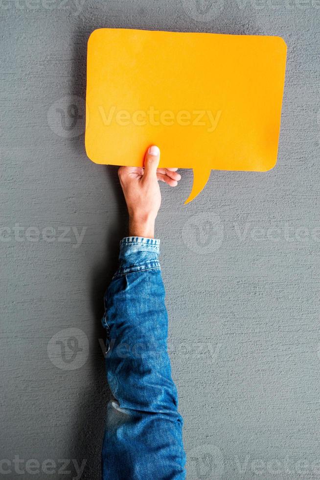 Write your thoughts. Close-up of man stretching out empty speech bubble against grey background photo