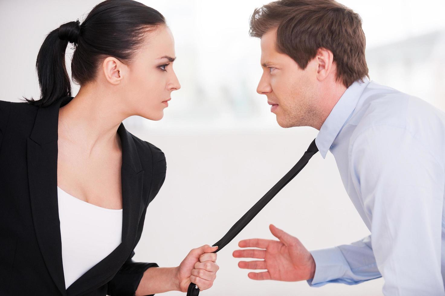 Business conflict. Young man and woman in formalwear looking at each other and expressing negativity while woman grabbing the necktie of her opponent photo