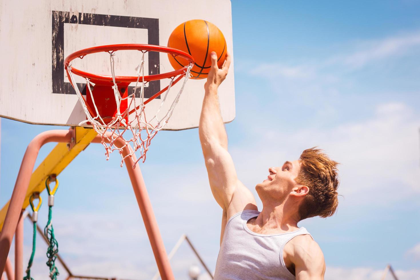 golpe de gracia. vista lateral del joven jugador de baloncesto haciendo slam dunk foto