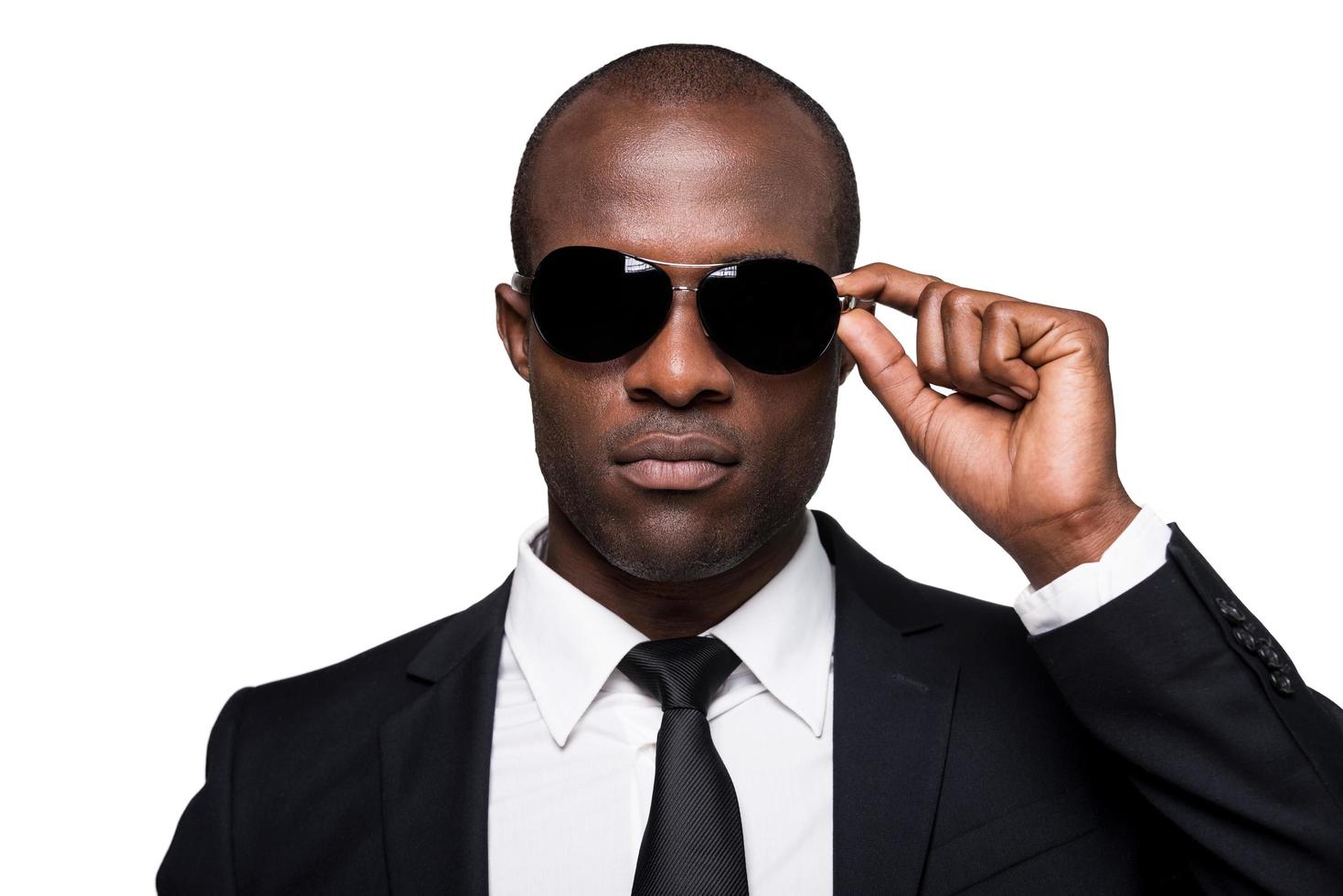 Cool handsome. Portrait of serious young African man in formalwear adjusting his sunglasses while standing isolated on white background photo