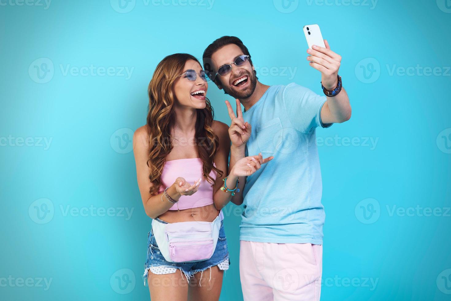 Beautiful young smiling couple making selfie while standing against blue background photo