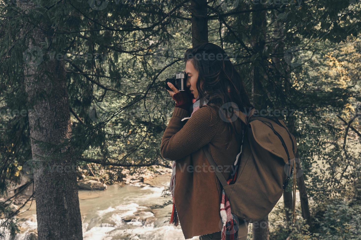 Collecting views. Young modern woman with backpack photographing nature while hiking in the woods photo