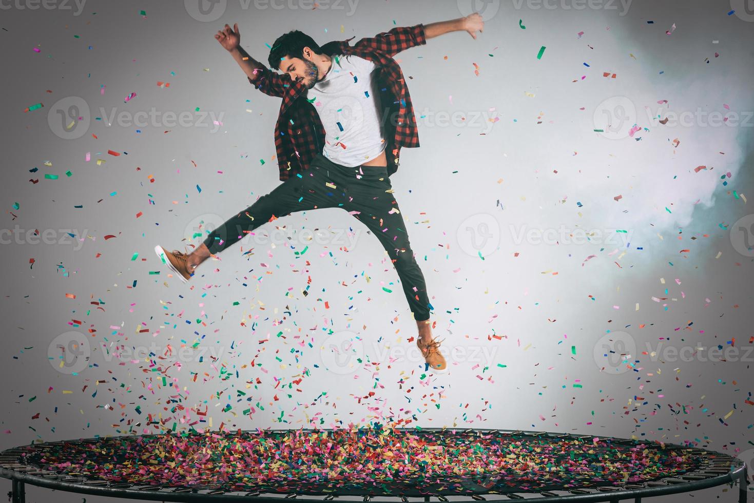 Unleashed fun. Mid-air shot of handsome young man jumping on trampoline with confetti all around him photo