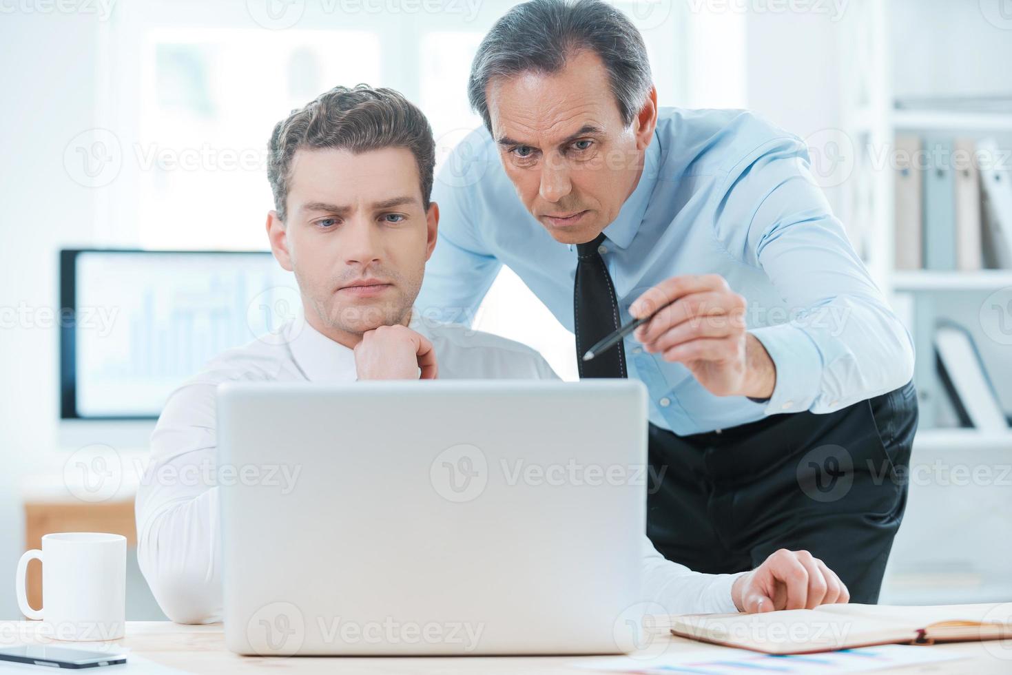 Sharing experience with colleague. Two serious business people in formalwear discussing something and looking at laptop photo