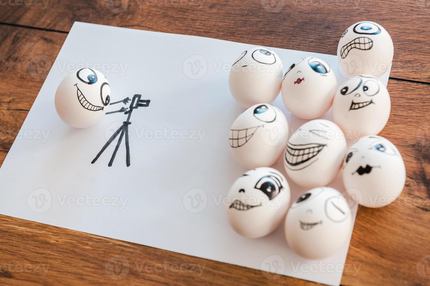 Together we are stronger. Top view of funny egg photographing his egg friends while all of them laying on the piece of paper and on the wooden desk photo