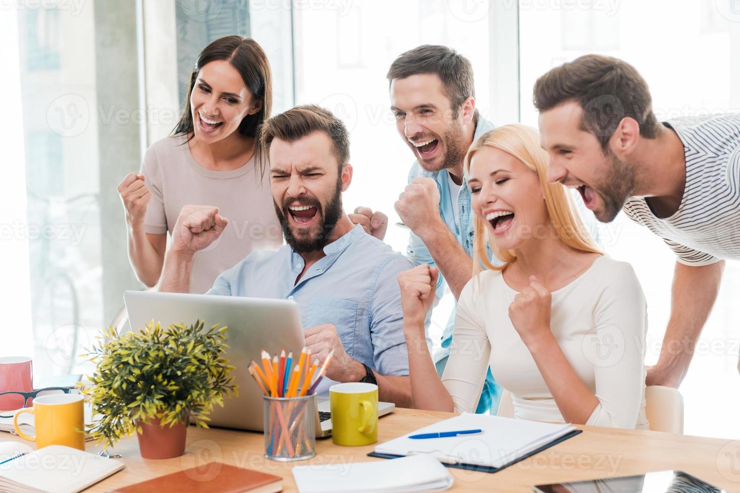 Everyday winners. Group of happy business people in smart casual wear looking at the laptop and gesturing photo