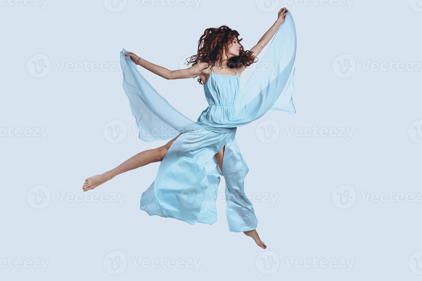 Feeling free to do anything. Full length studio shot of attractive young woman in elegant dress keeping arms outstretched while hovering against grey background photo