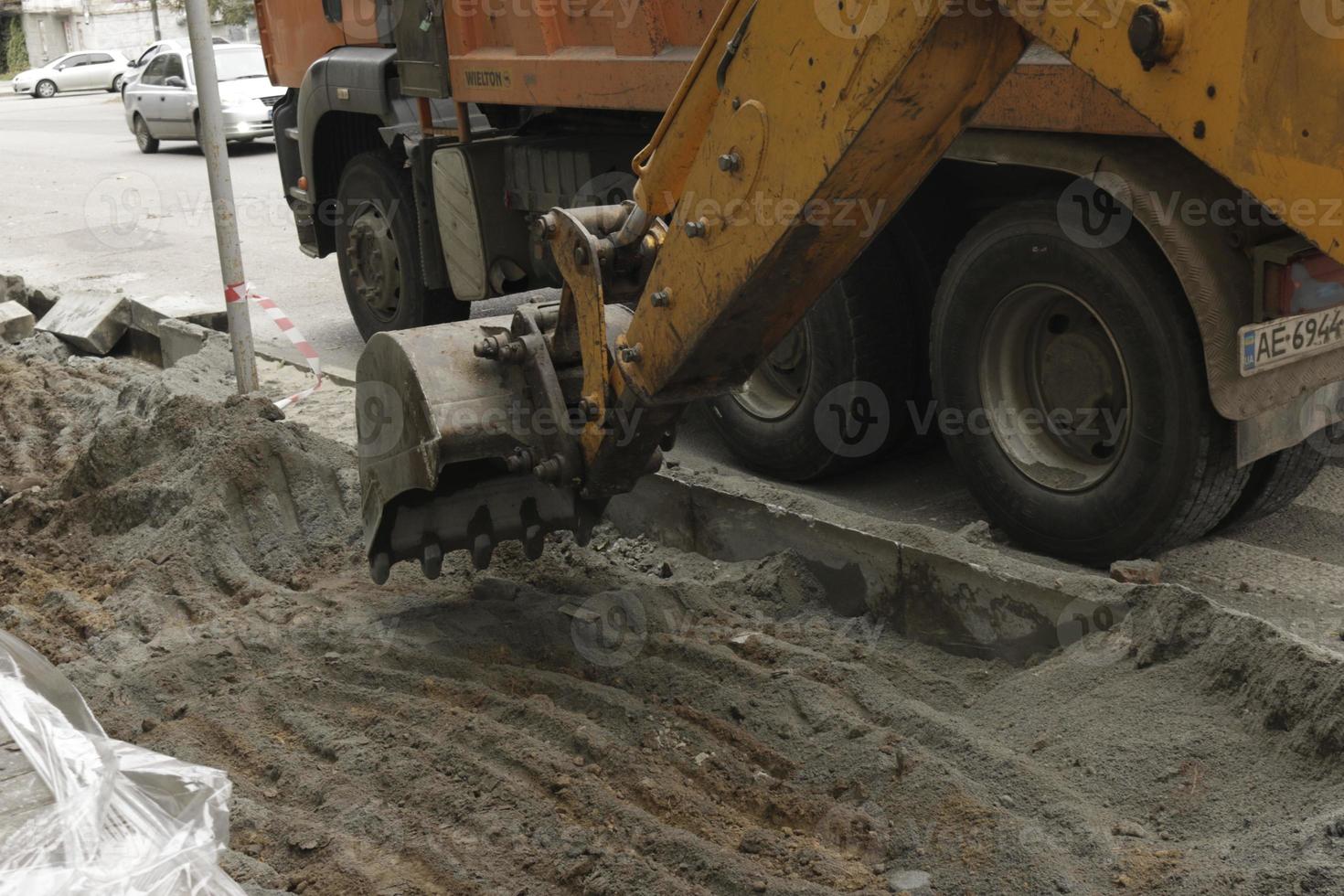 Road works on the city street. The excavator bucket collects the old pavement and loads it into a dump truck. photo