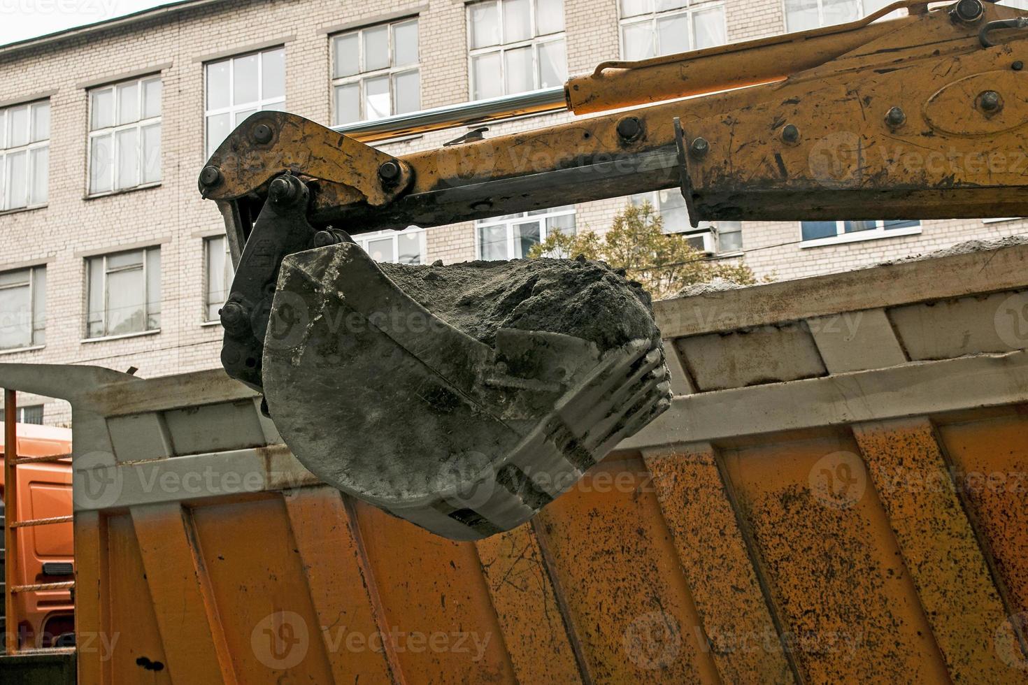 Road works on the city street. The excavator bucket collects the old pavement and loads it into a dump truck photo