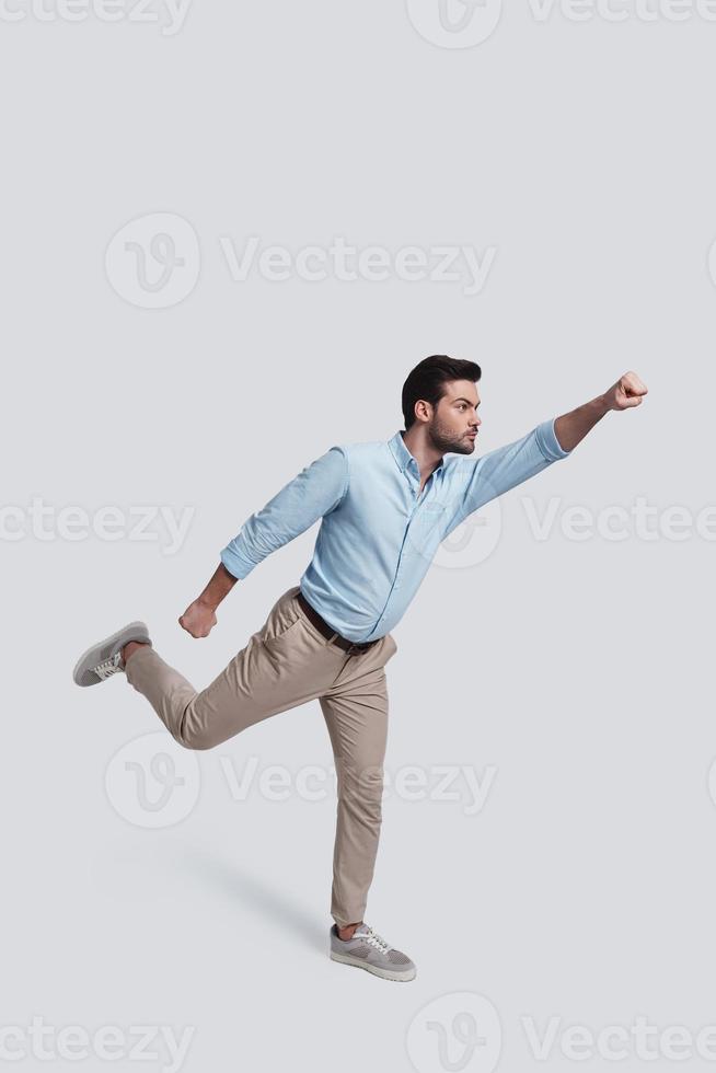 Real hero.  Full length of handsome young man gesturing while standing against grey background photo