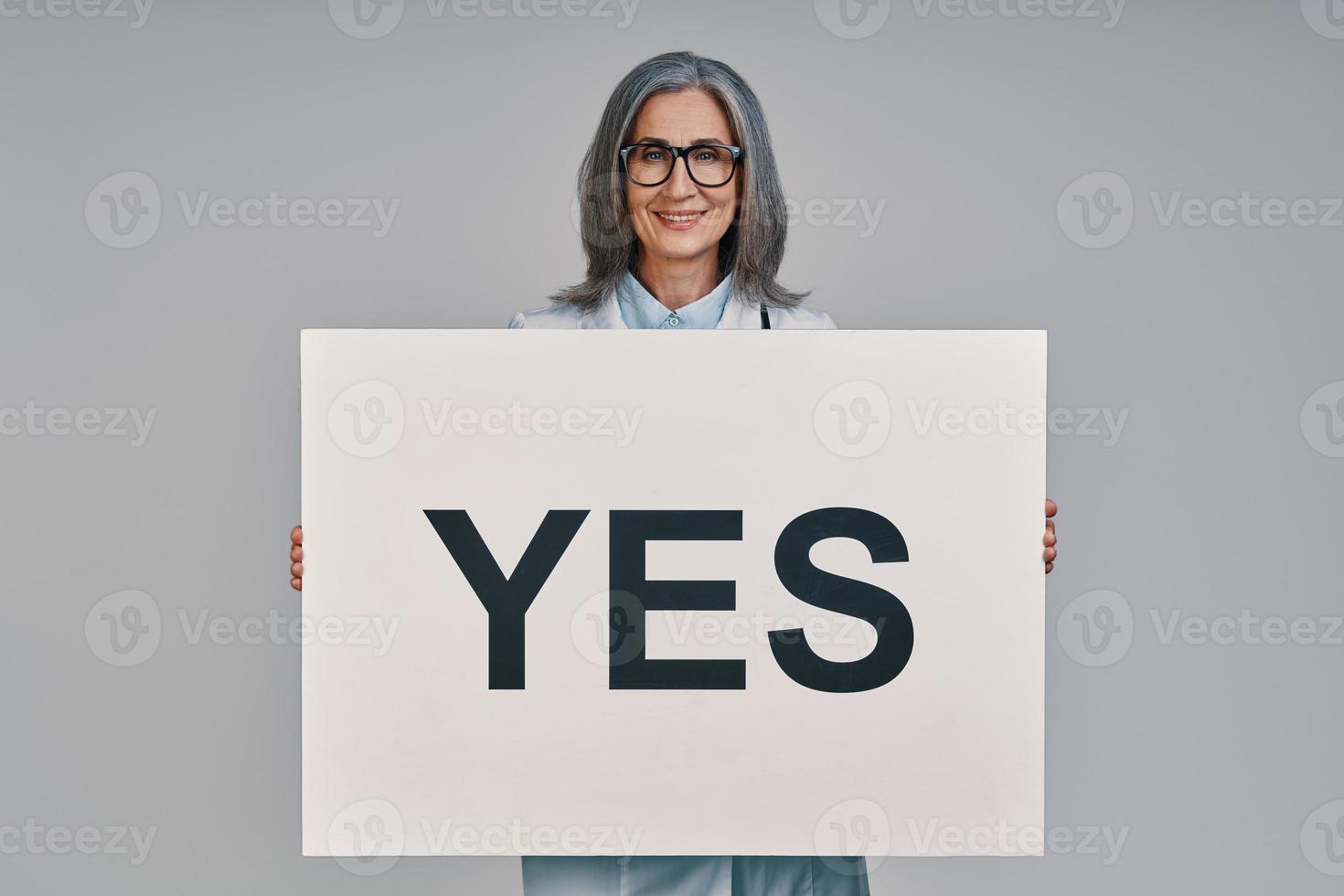 Mature beautiful female doctor looking at camera and holding placard photo