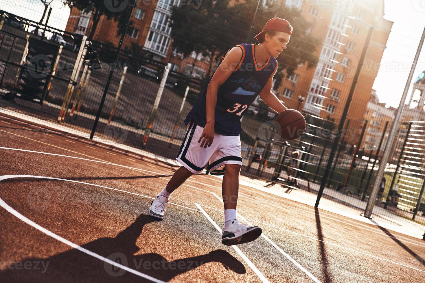 Carefree game. Full length of young man in sports clothing playing basketball while spending time outdoors photo