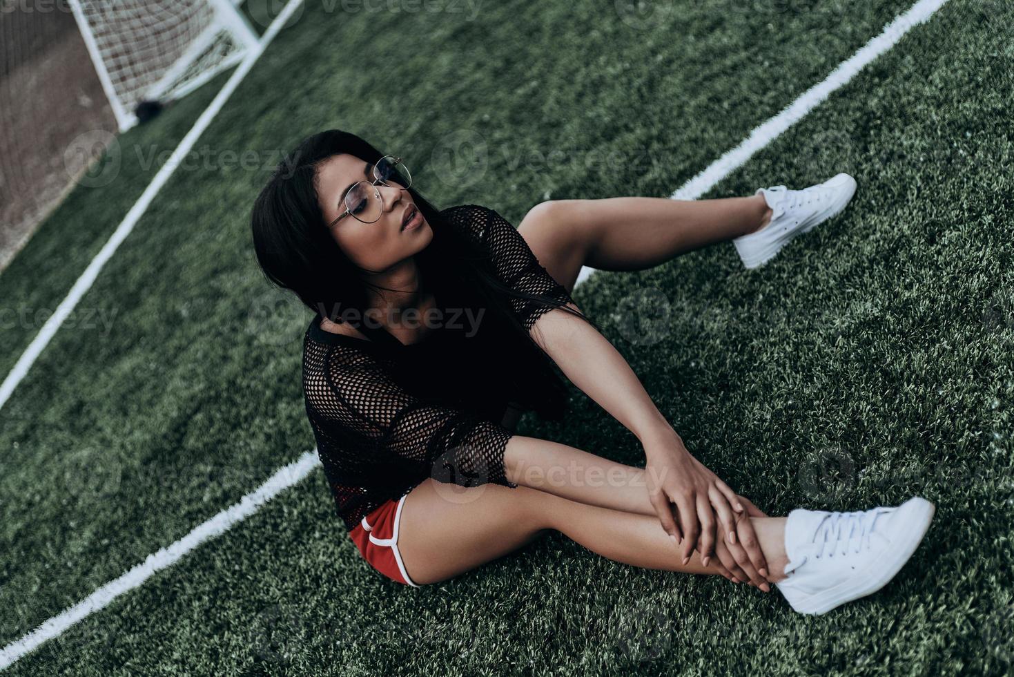 Seductive player. Beautiful young mixed race woman in sport clothing sitting on the soccer field photo