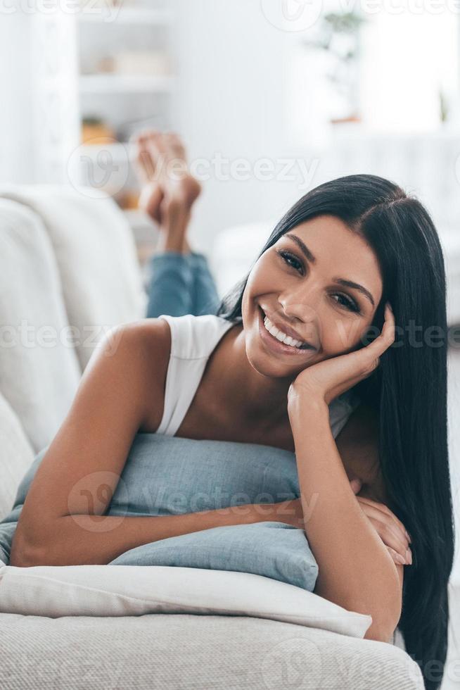 Resting at home. Young beautiful woman looking at camera and smiling while lying on the sofa at home photo